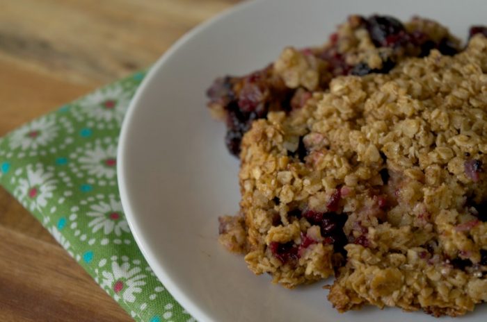 Mixed berry baked oatmeal on white serving dish that is sitting on a green floral napkin on a wooden table