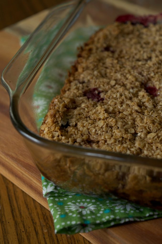 Mixed berry baked oatmeal in glass baking dish resting on green floral napkin on wooden table