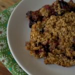 Mixed Berry Baked Oatmeal displayed on a white plate with green floral napkin underneath while sitting on a wooden table.
