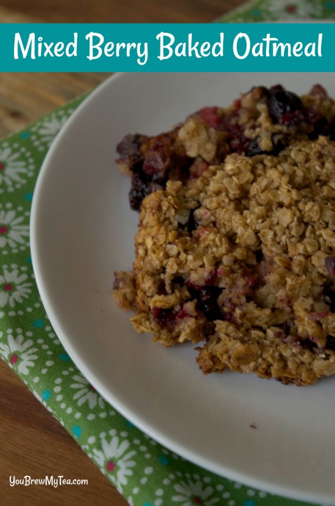 Mixed Berry Baked Oatmeal displayed on a white plate with green floral napkin underneath while sitting on a wooden table. 