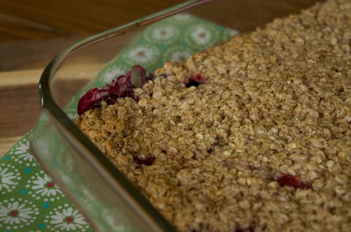 Mixed berry baked oatmeal in glass baking dish resting on green floral napkin on wooden table