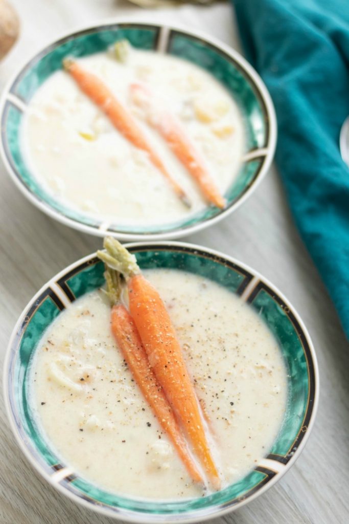 two teal and white bowls filled with creamy vegetable soup and sitting on as light colored surface with teal napkin in the background