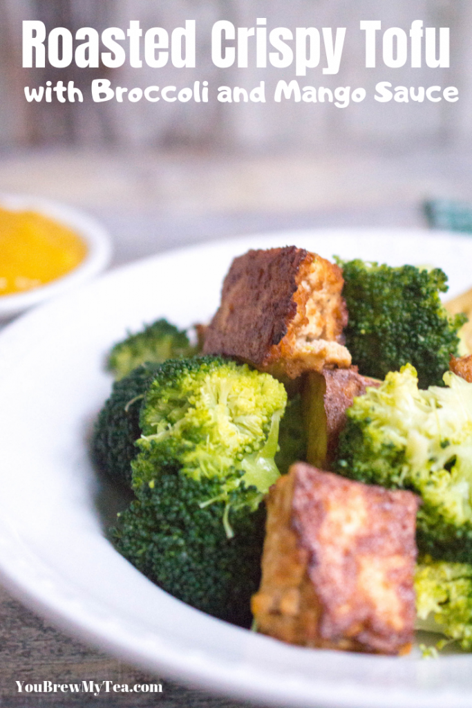 Roasted crispy tofu in a large white bowl alongside broccoli sitting on a countertop with a small bowl of mango sauce in the background