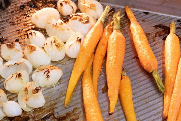 Roasted onions and carrots laying on a baking sheet