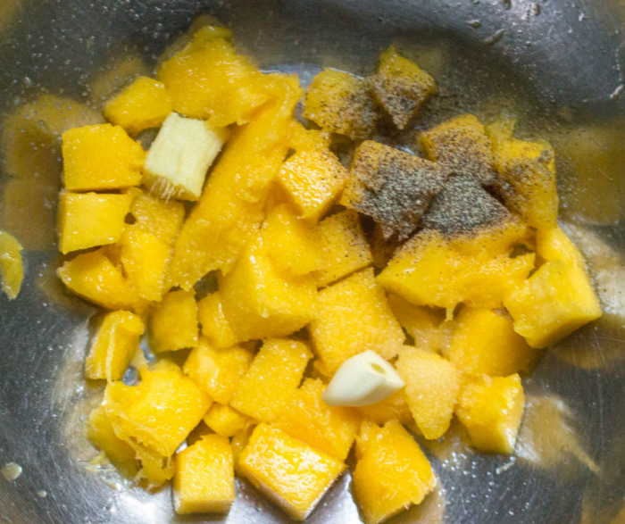 Diced mango and seasonings in a large stainless steel bowl to blend for the mango sauce that accompanies the crispy tofu and broccoli recipe