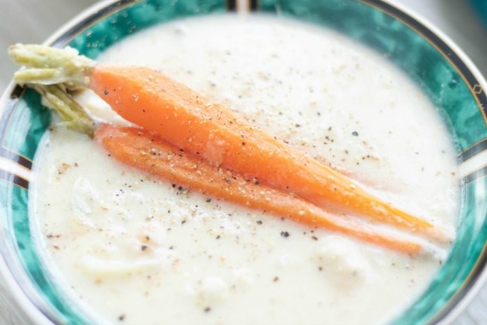 two teal and white bowls filled with creamy vegetable soup and sitting on as light colored surface with teal napkin in the background