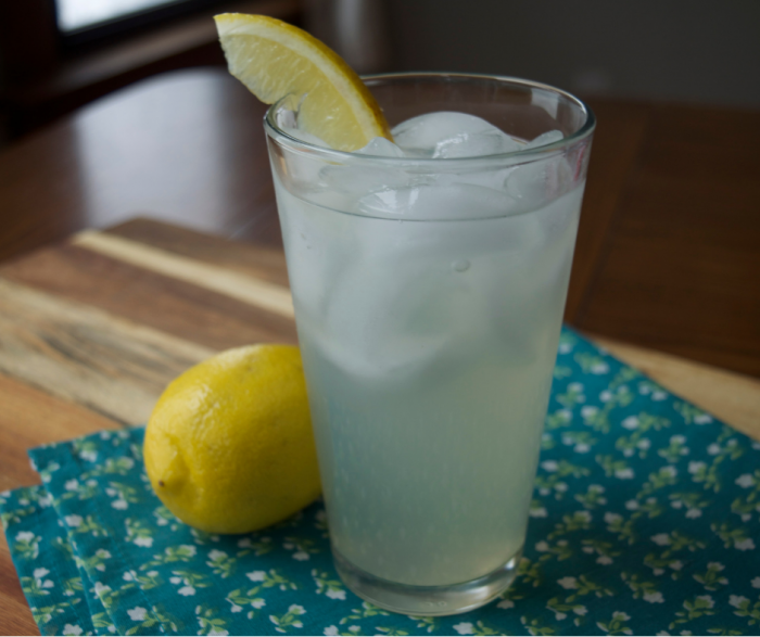 A tall glass of sugar free lemonade sitting on a wooden table and teal napkin with small flowers