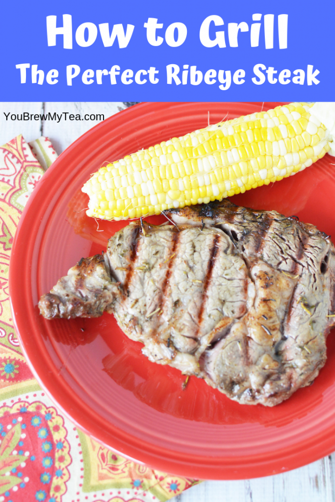 Grilled ribeye steak laying on s red plate that is sitting on a colorful napkin with an ear of corn sitting on the plate