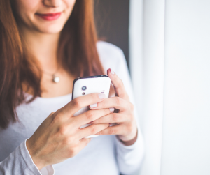 Women holding a smartphone in front of a window with white curtains