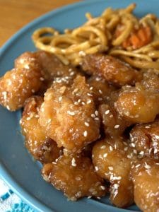 sesame chicken on teal plate with noodles