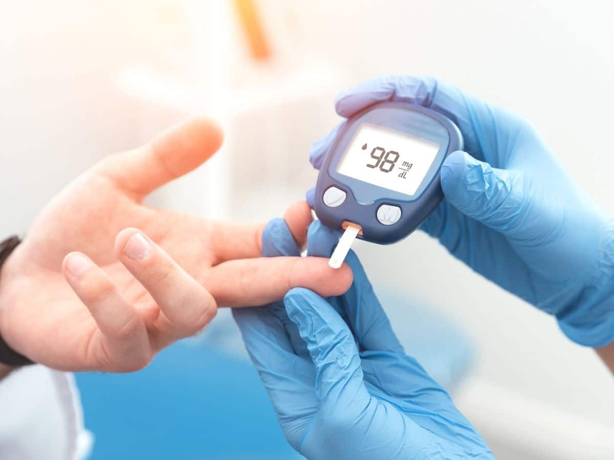 gloved hand holding glucose meter to finger