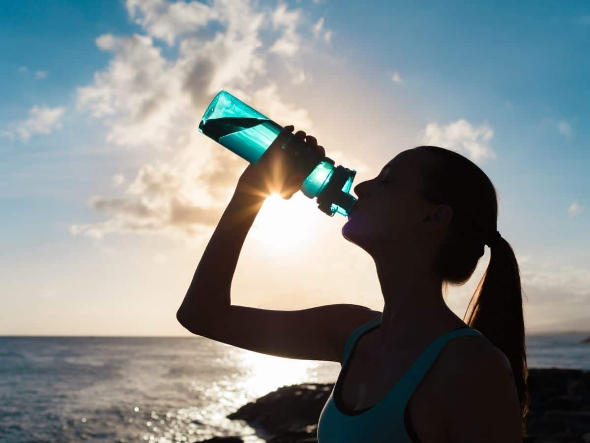 woman drinking from water bottle in front of body of water