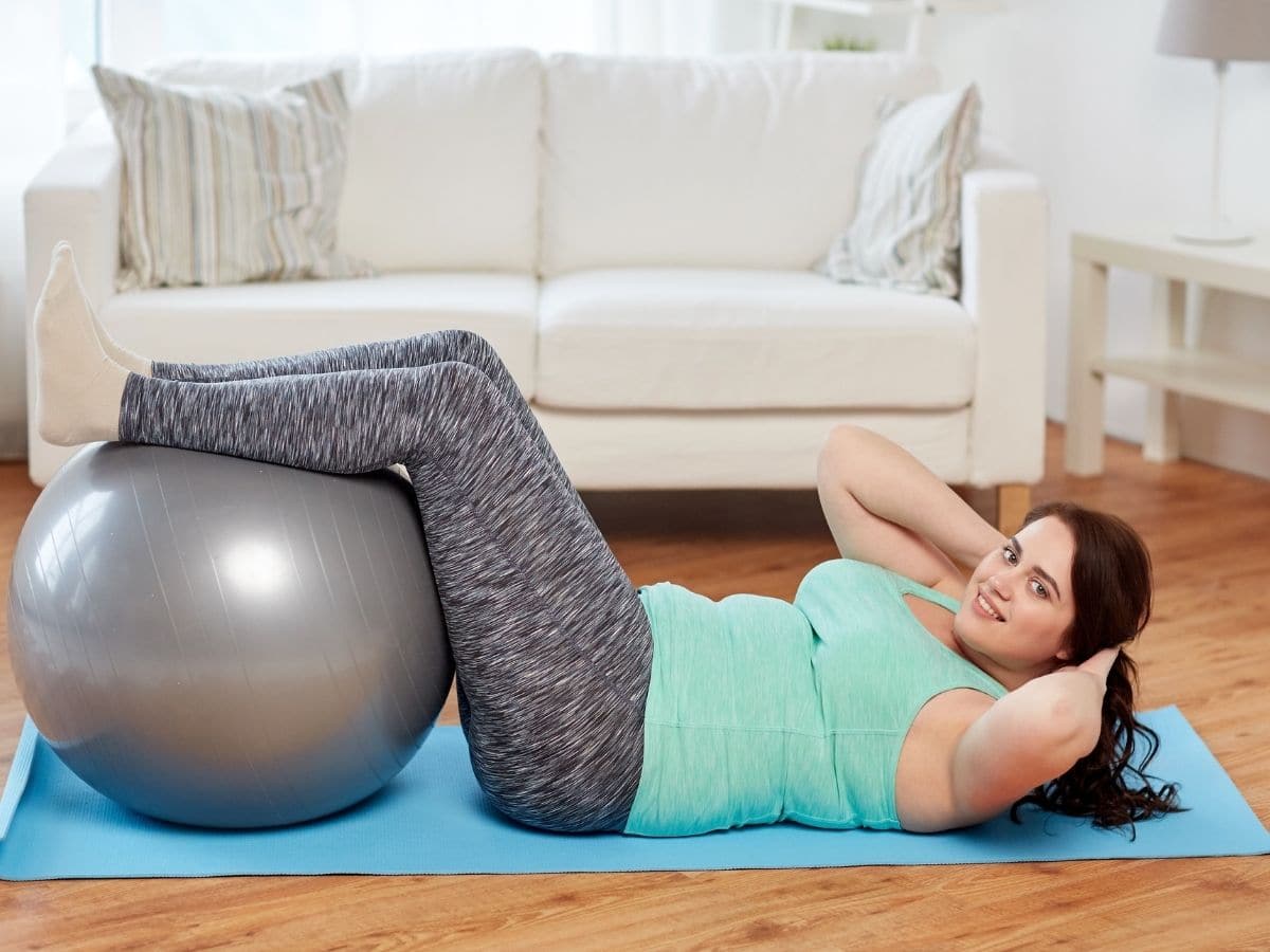 woman in gray and green doing a sit up with exercise ball