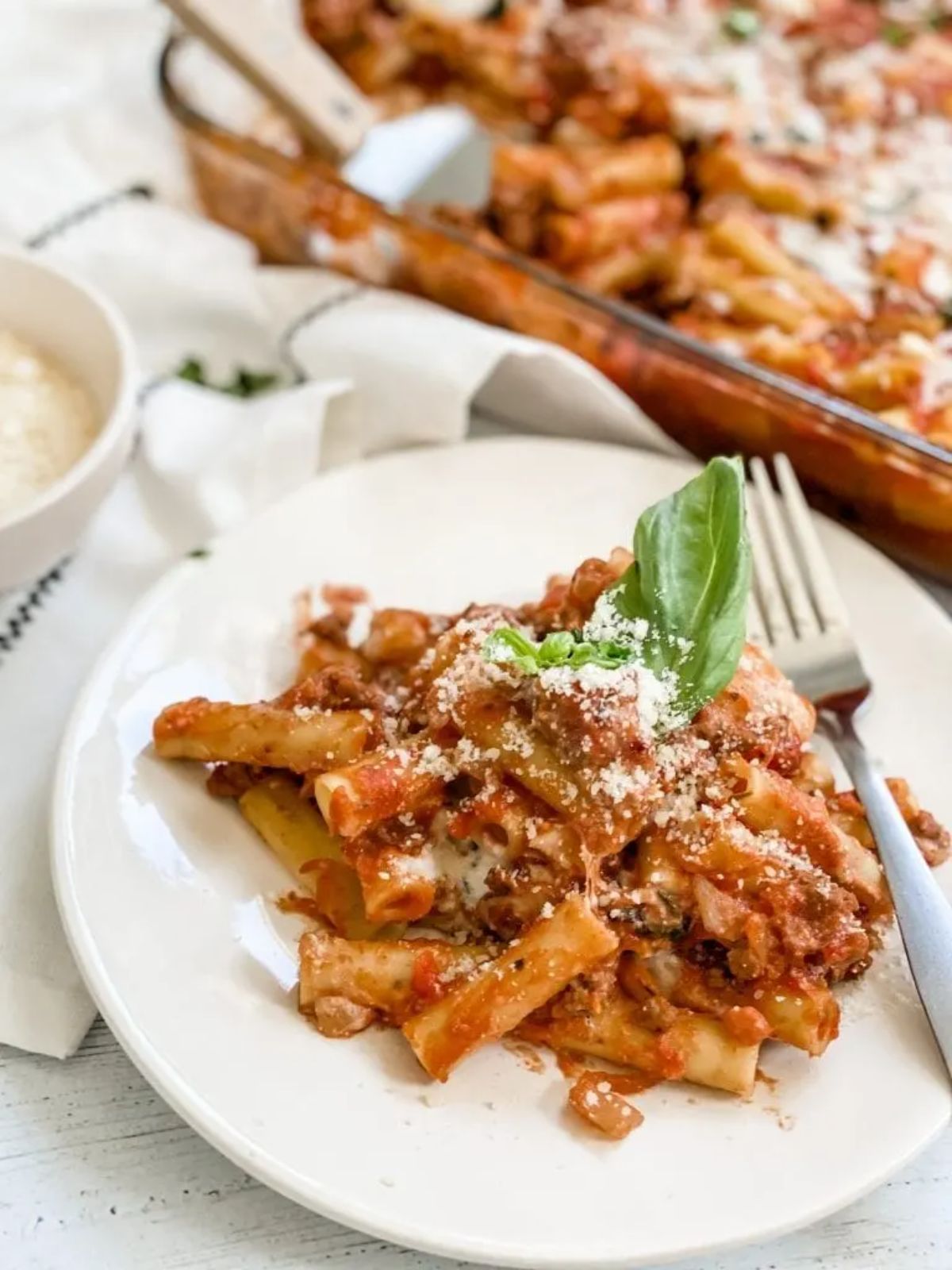 pasta on white plate next to baking dish of baked ziti