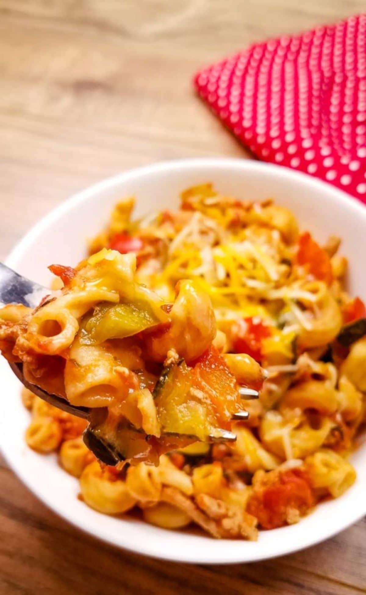 forkful of pasta above white bowl on table with pink napkin