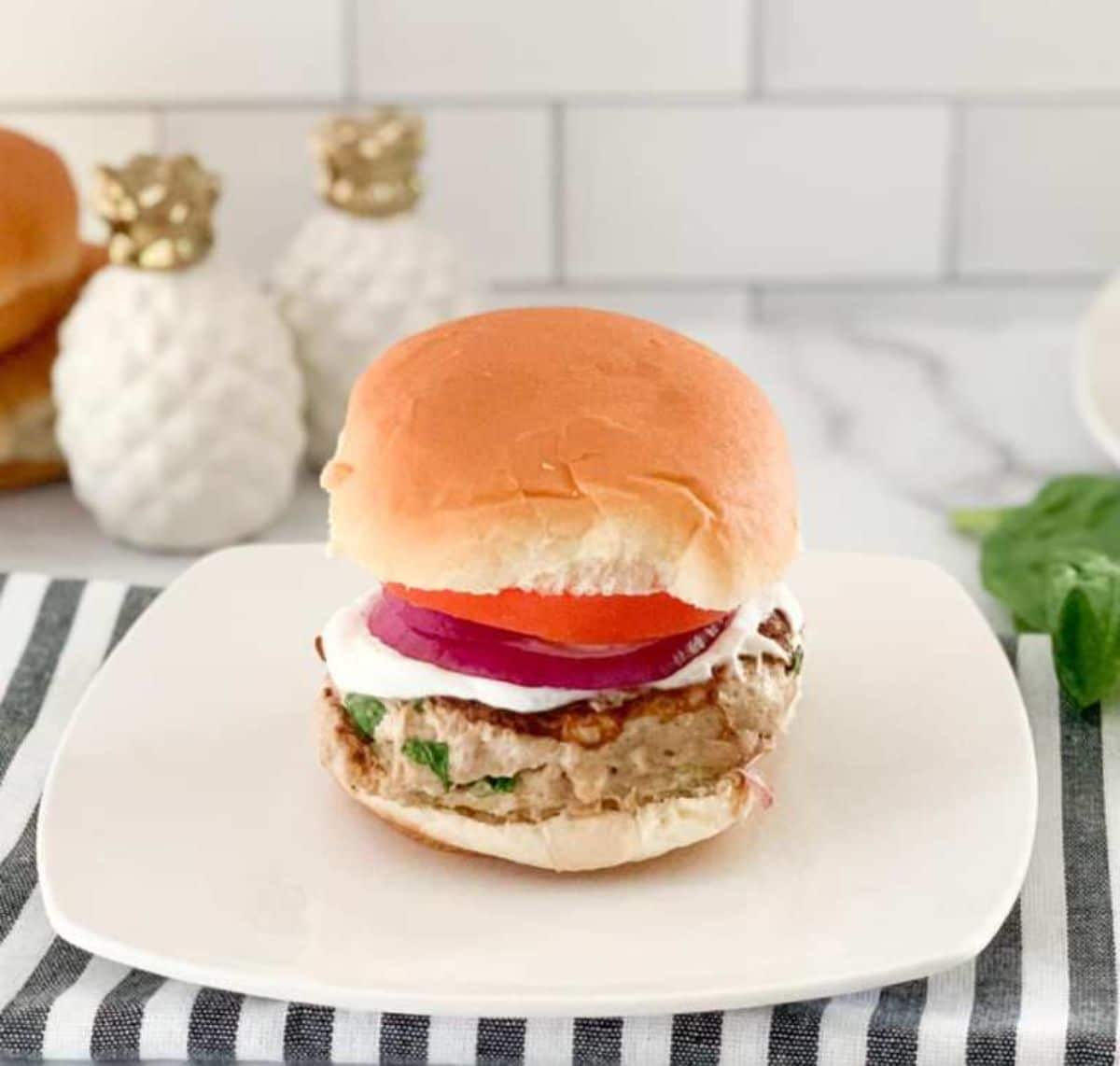 burger on white square plate over striped napkin