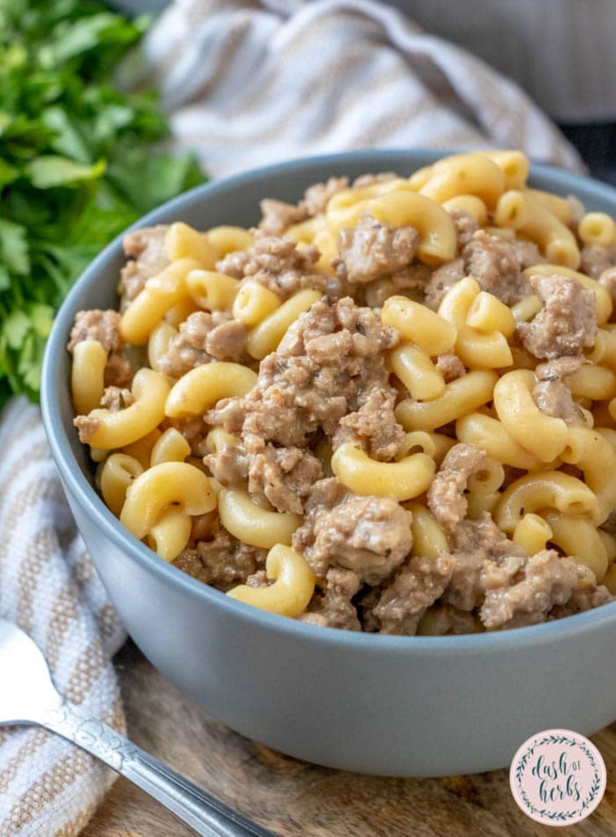 pasta with ground meat in light blue bowl next to striped napkin