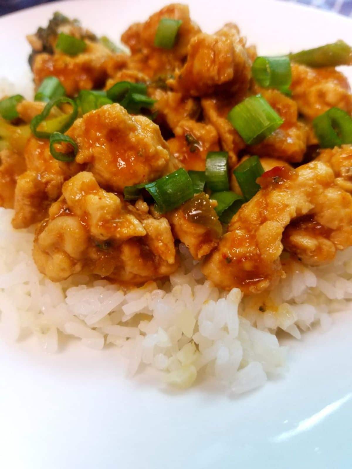 firecracker chicken with onions on top of rice on white plate