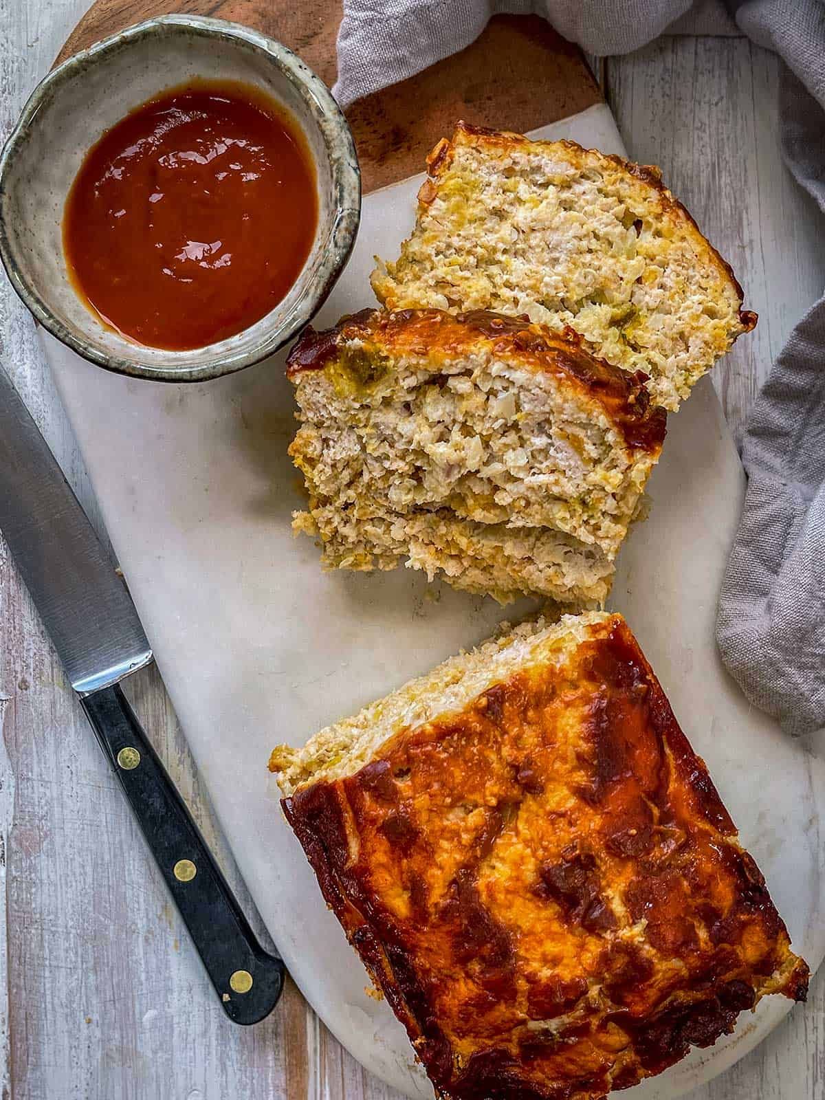 meatloaf sliced on white board next to knife and bowl of ketchup