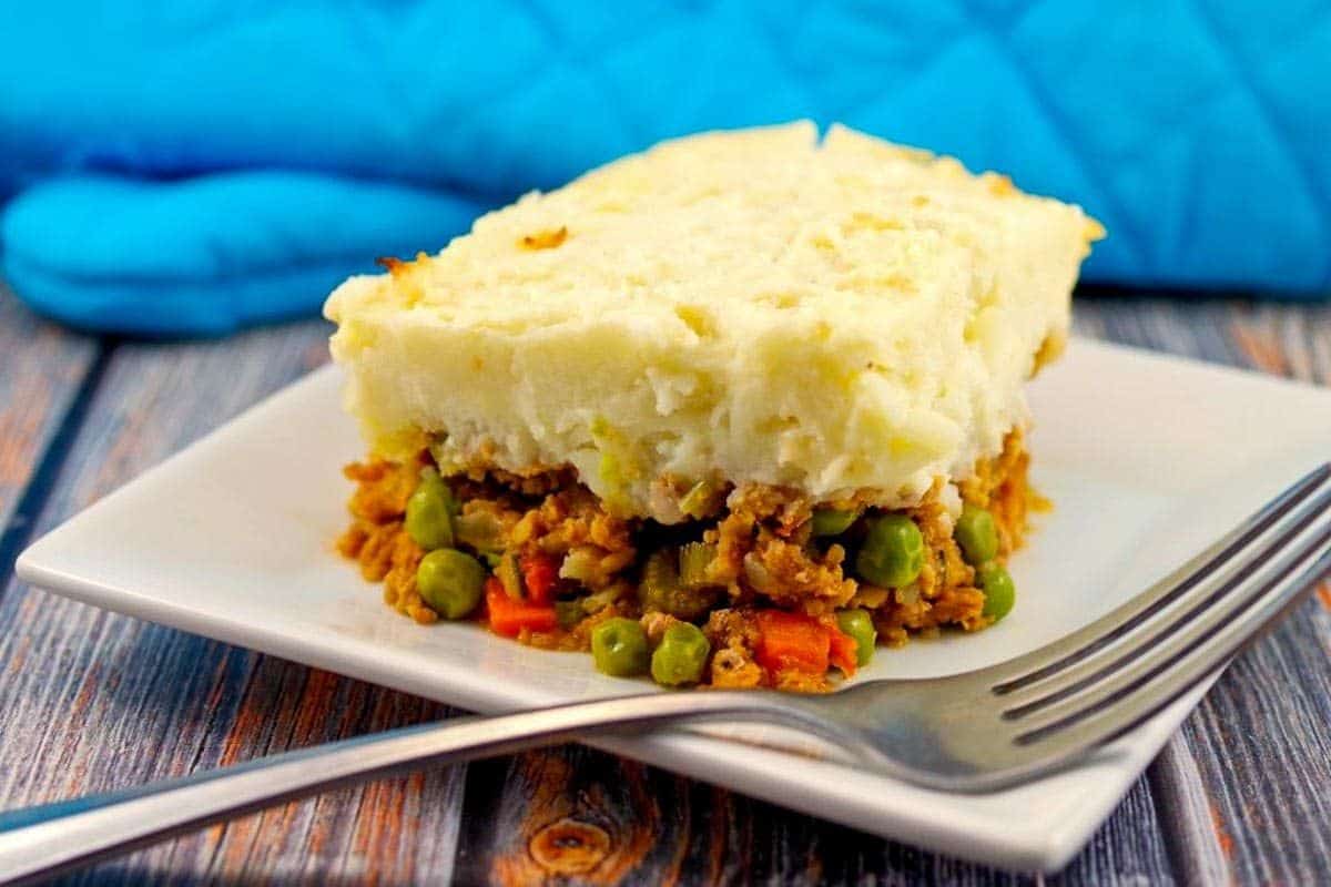 slice of shepherds pie on white plate with blue napkin in background