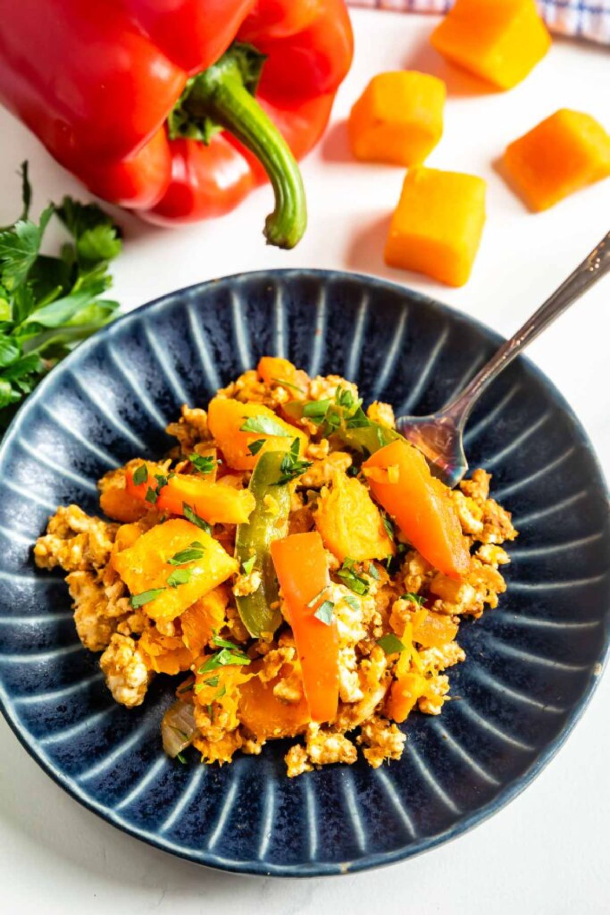 ground turkey and butternut squash in blue round plate by red bell pepper