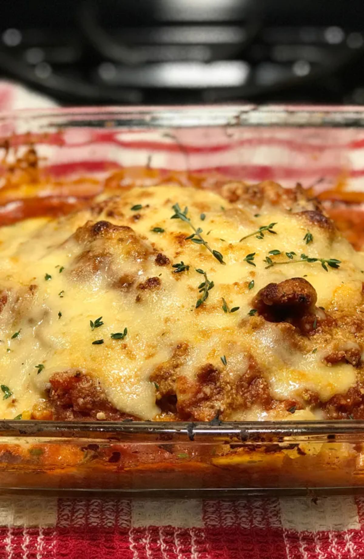 casserole topped with cheese in glass dish on checked tablecloth