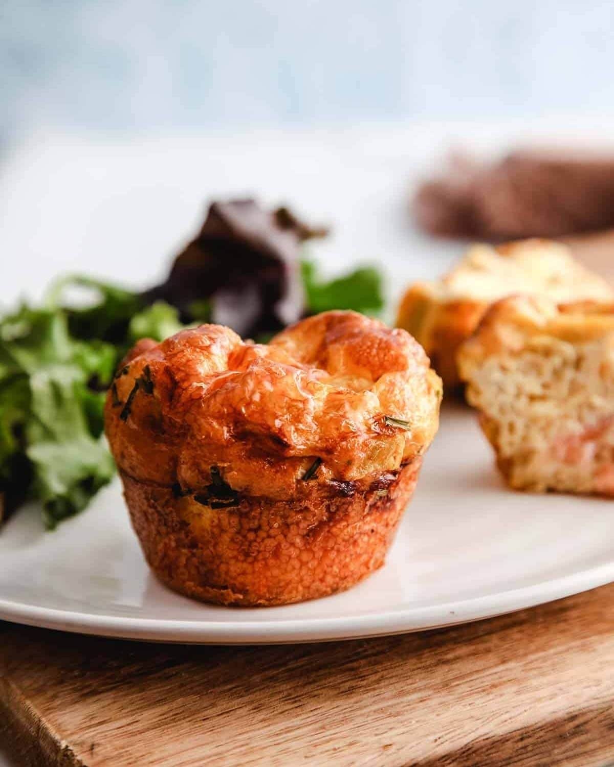 muffin on white plate with greens in background