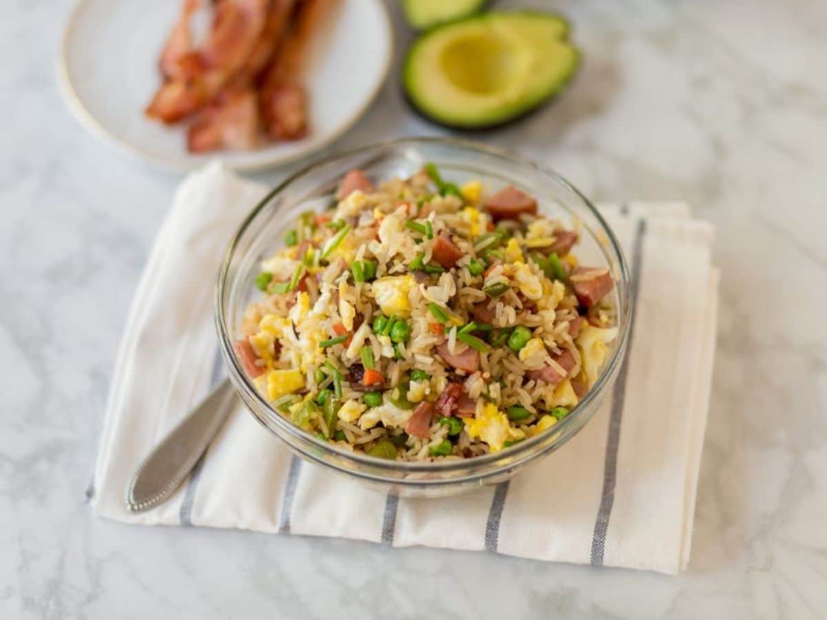 glass bowl of fried rice on white striped napkin with half avocado in background