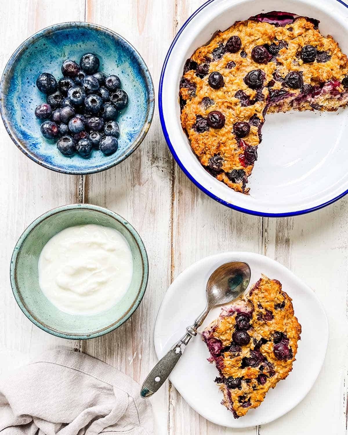 blueberry cake on white plate by green bowl of yogurt