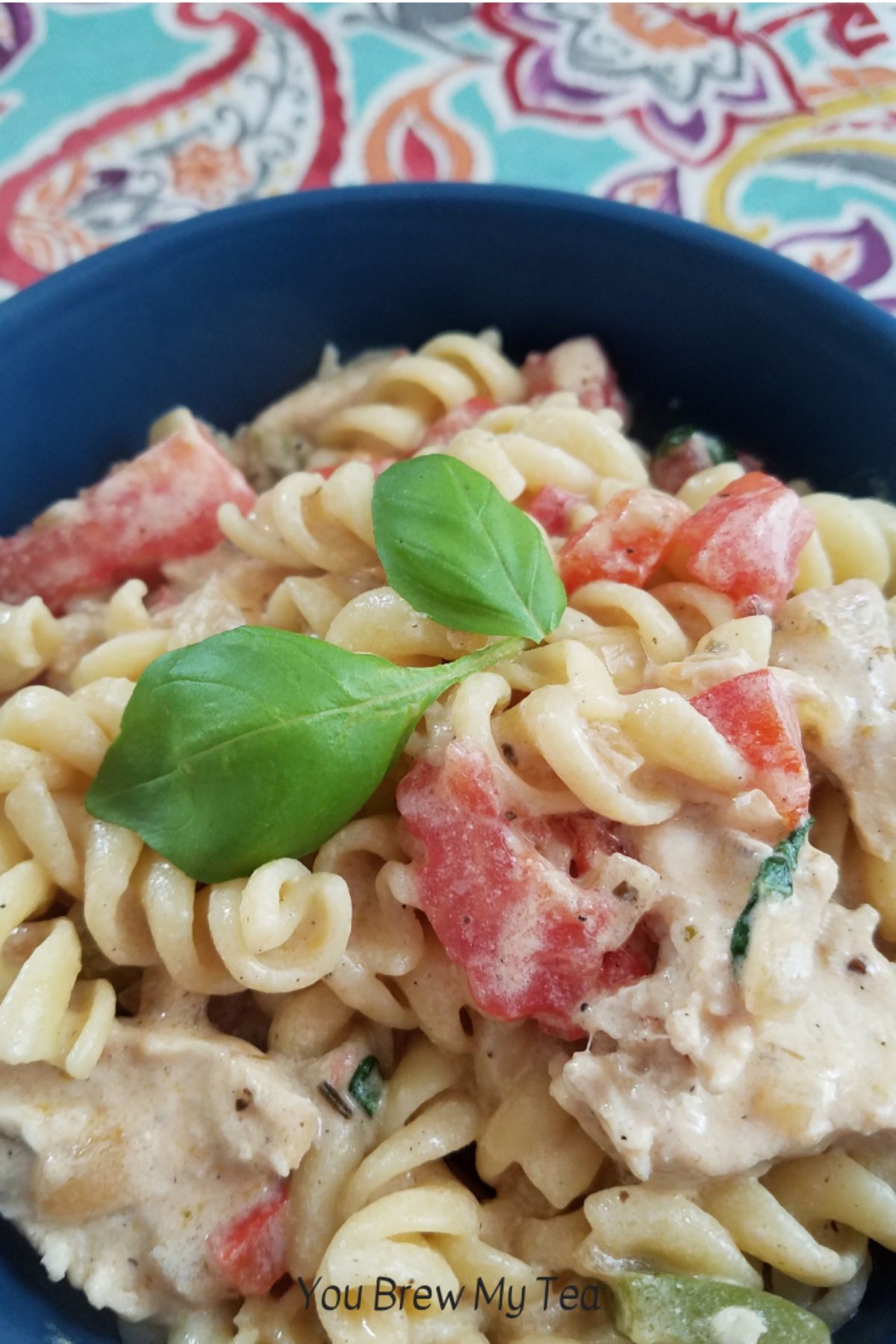 pasta in blue bowl topped with tomato and basil