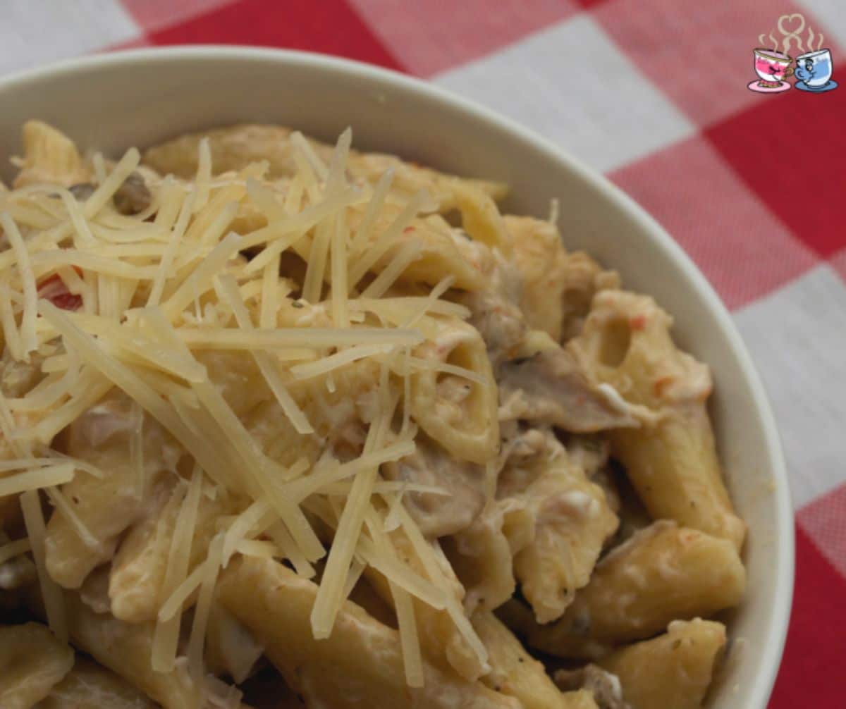 white bowl of pasta with parmesan on top sitting on red and white napkin