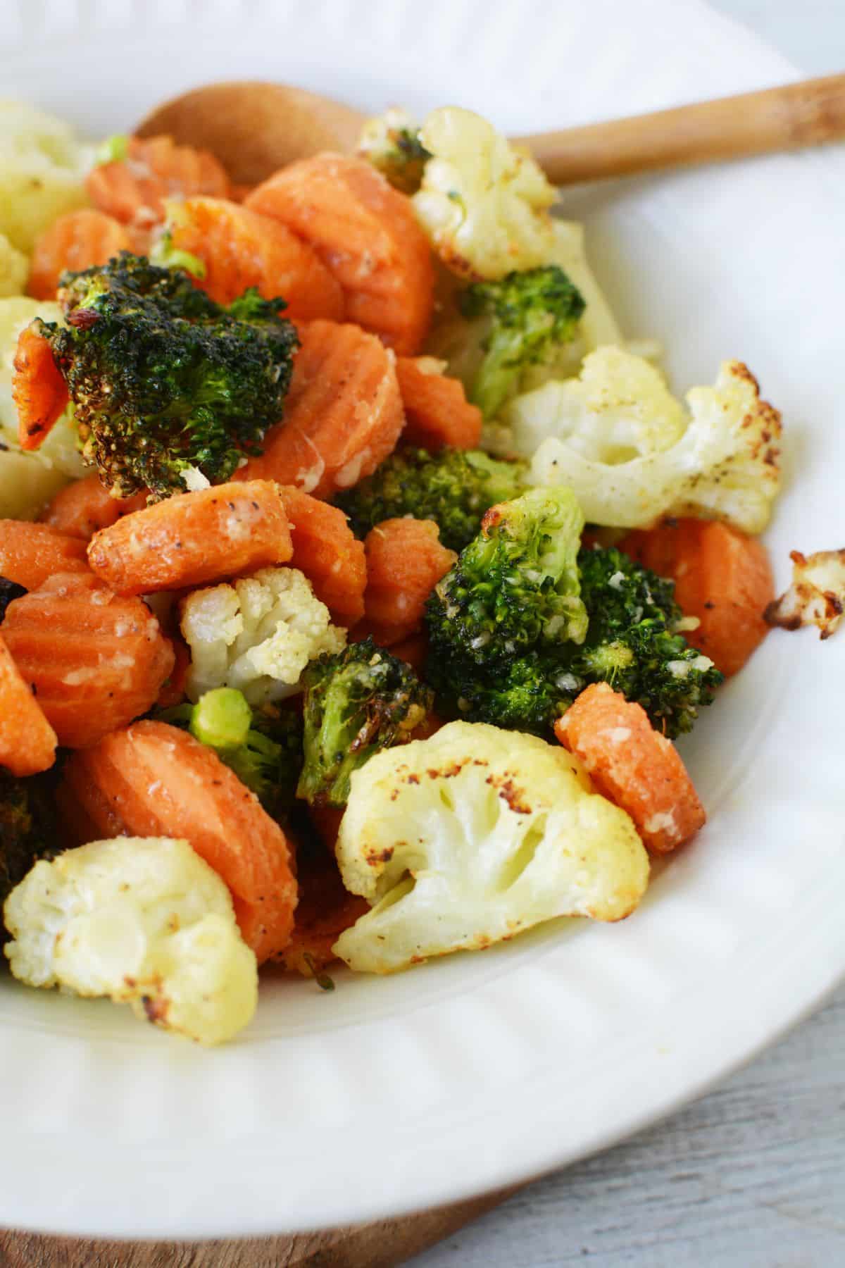 wooden spoon at top of white bowl filled with parmesan vegetables