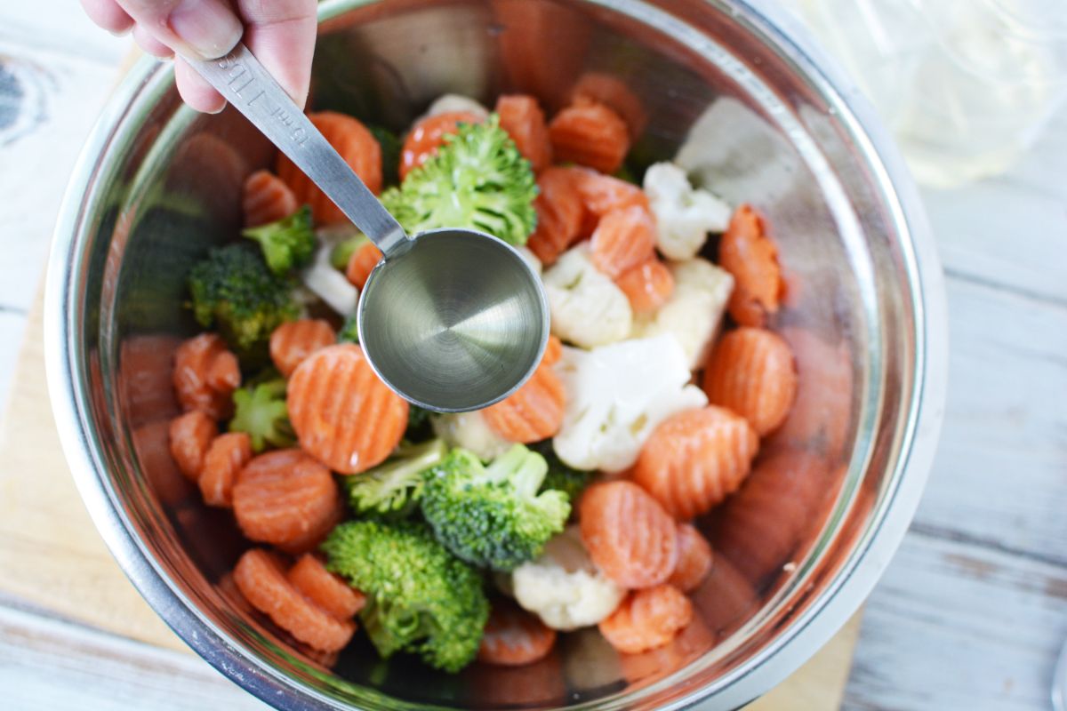 spoon of olive oil held above bowl of veggies